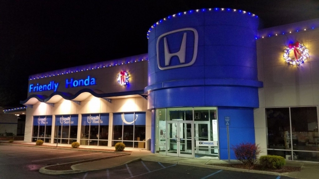 Exterior of a Honda dealership at night with holiday decorations and illuminated signs.