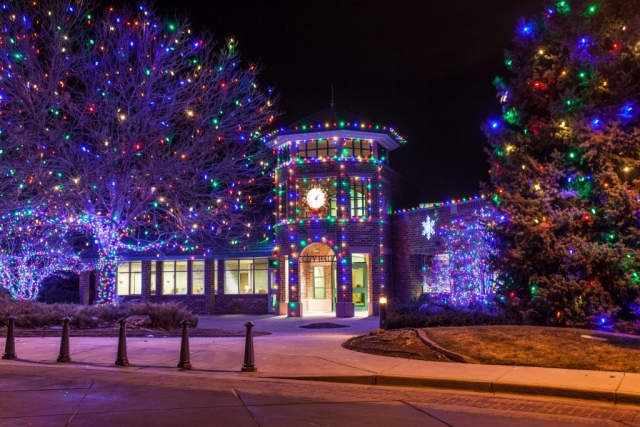 Brick building and trees decorated with colorful holiday lights at night.