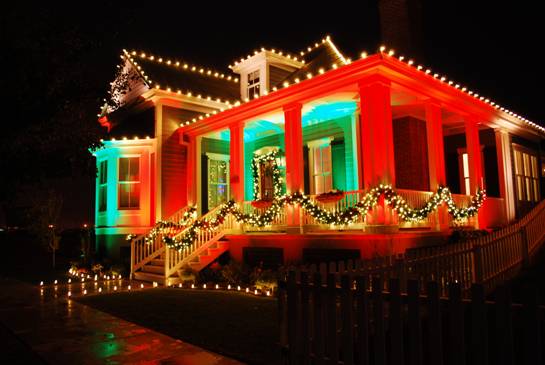 A house decorated with red, green, and white lights for the holidays, featuring garlands and illuminated pathways.