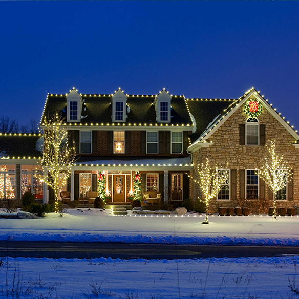 A house decorated with Christmas lights, including illuminated trees and wreaths, on a snowy evening.