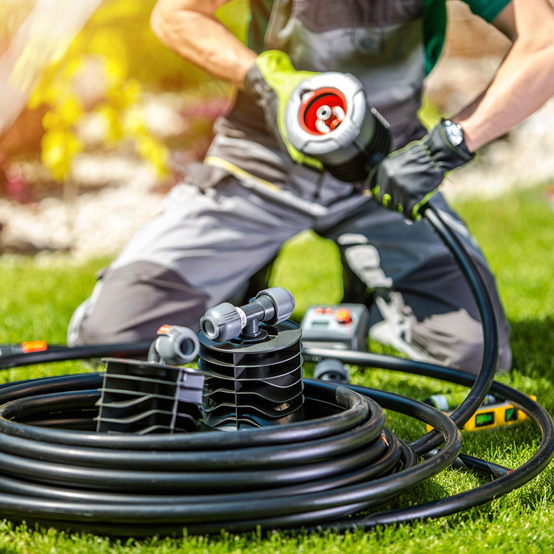 Person assembling a water hose and fittings outdoors on grass.