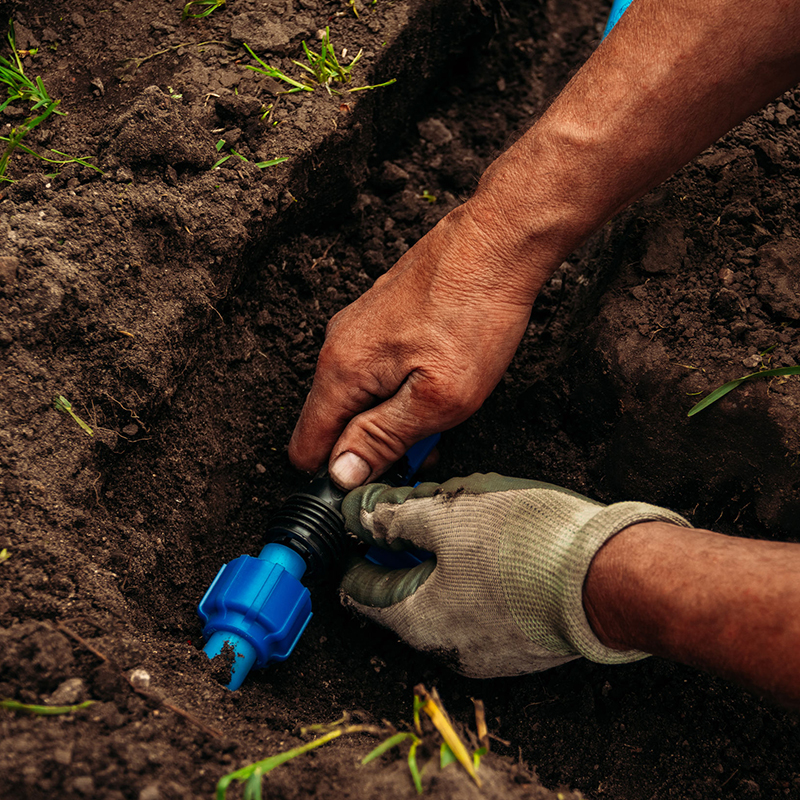 Hands connecting a blue plastic pipe fitting in soil.