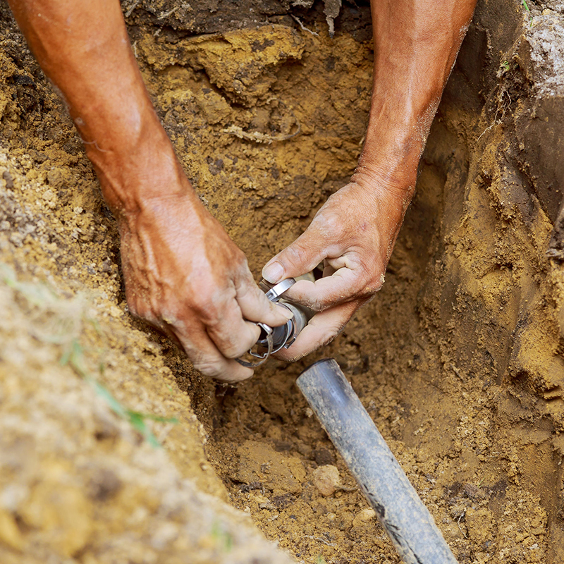 Person fixing underground plumbing with hands in a dirt hole.